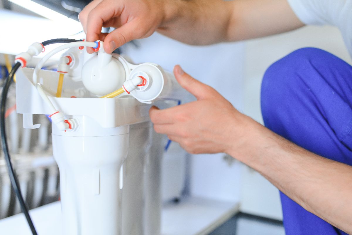 Technician installing or servicing a reverse osmosis water filtration system with connected purification components and tubing.
