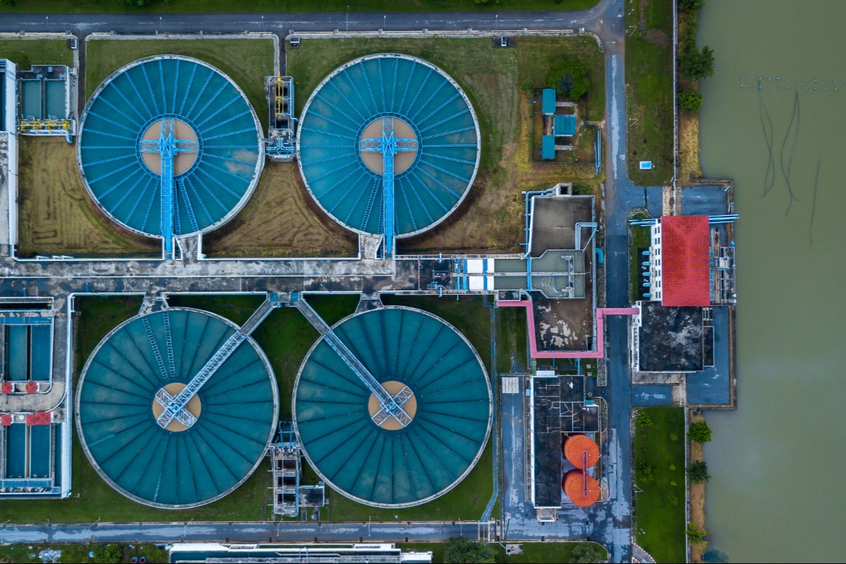 Aerial view of a large-scale wastewater treatment facility with circular clarifier tanks and industrial water processing systems.