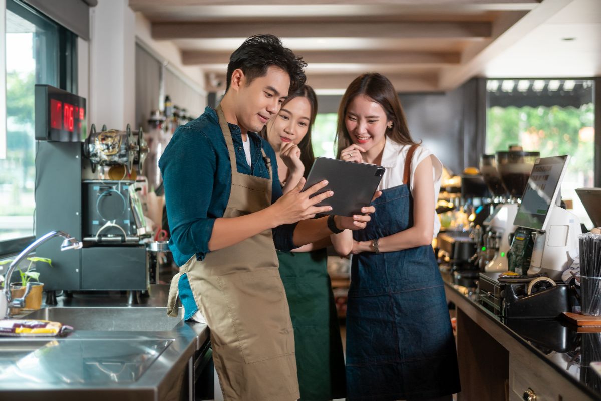 Café staff reviewing operations on a tablet inside a coffee shop with commercial beverage equipment and water filtration systems.