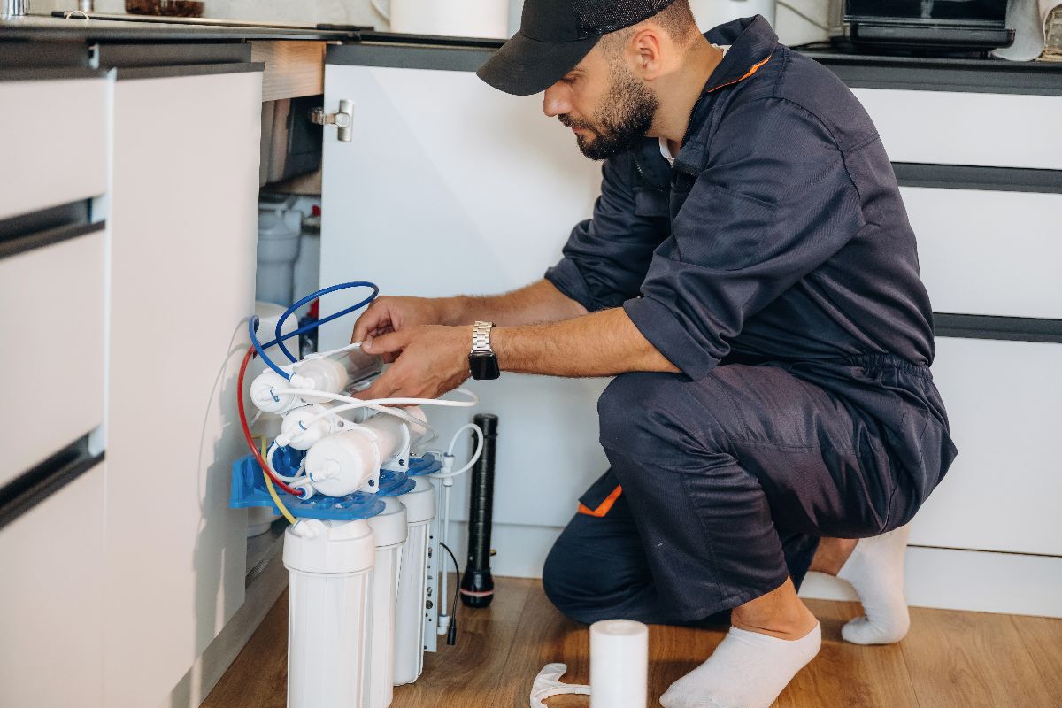 Technician installing or servicing an under-sink reverse osmosis water filtration system in a residential kitchen.