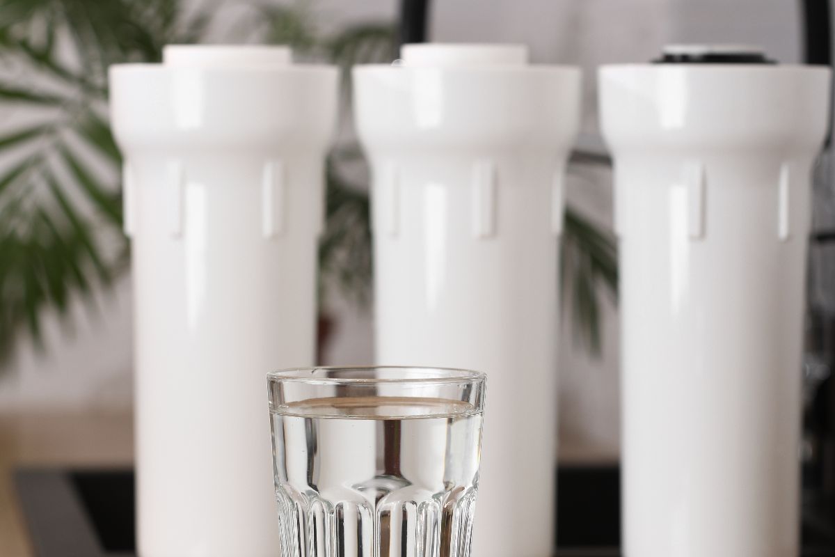 Glass of water in front of three white filtration housings for a water treatment system