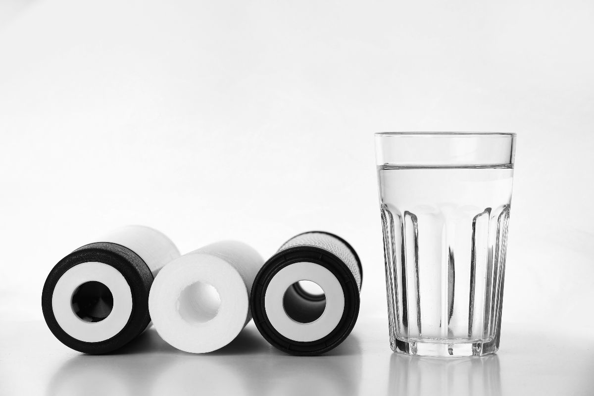 Water filter cartridges beside a glass of water on a clean white surface