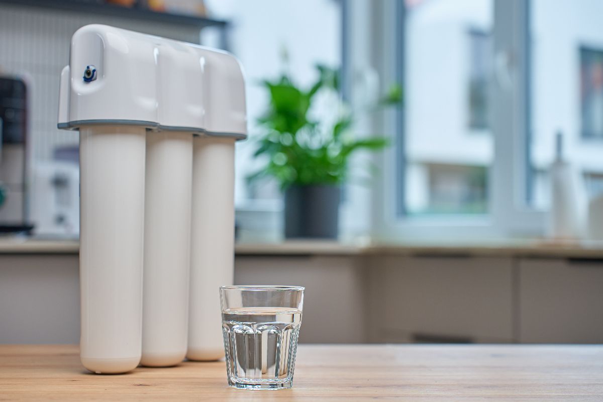 Three-stage water filtration system beside a glass of water on a kitchen counter