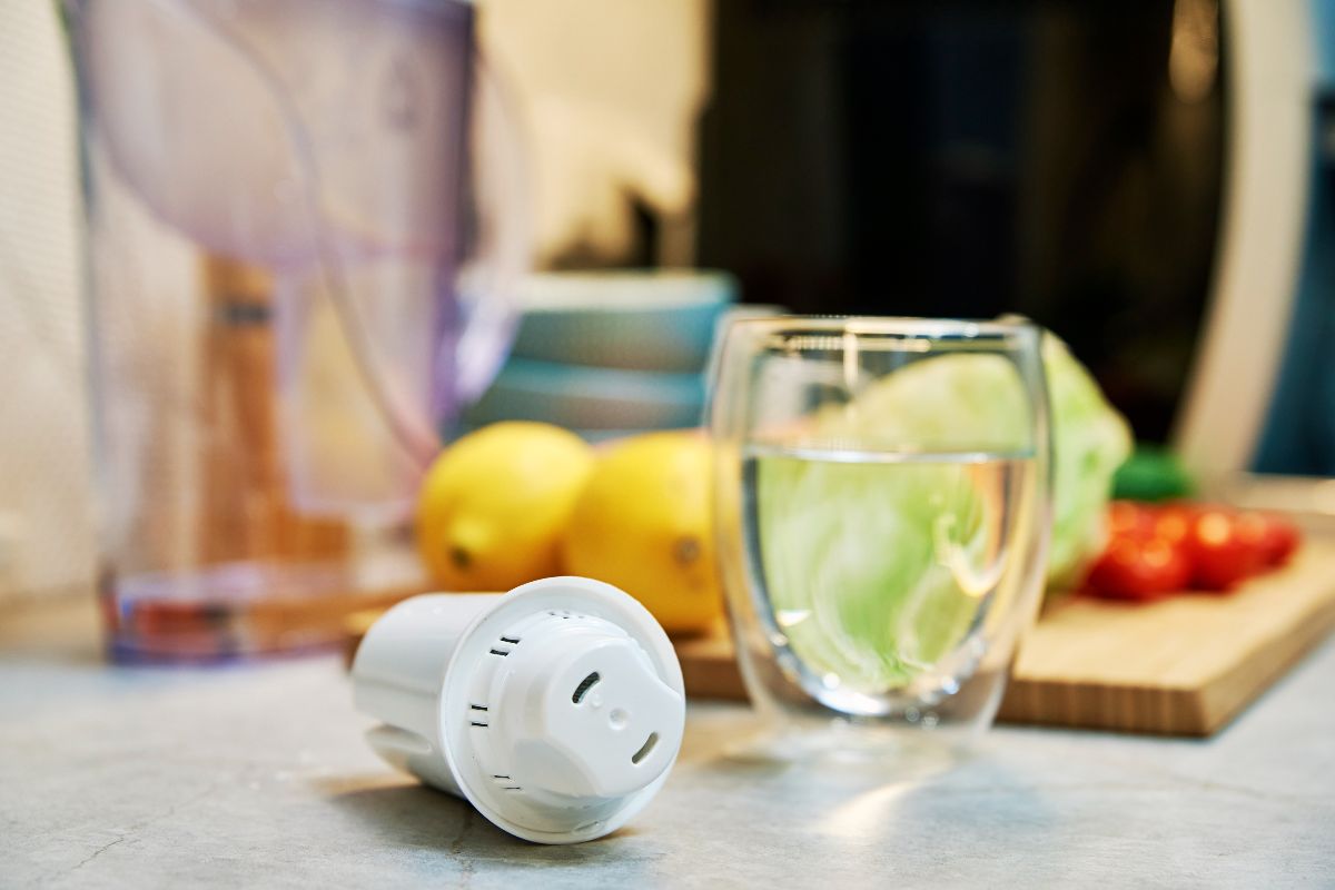 Water filter cartridge beside a glass of water and fresh ingredients in a kitchen
