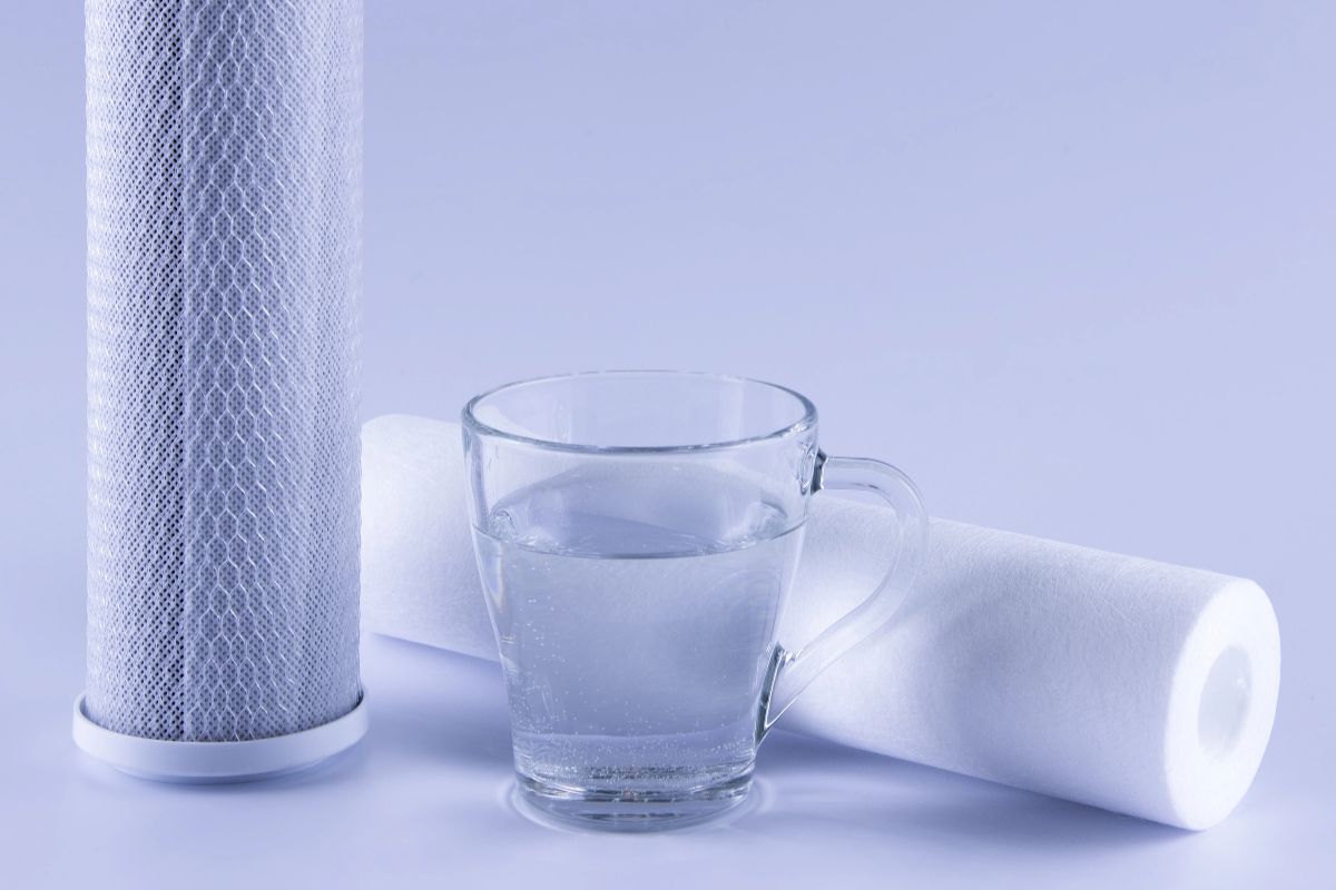 Reverse osmosis filter cartridges beside a clear glass mug of water on a light blue background