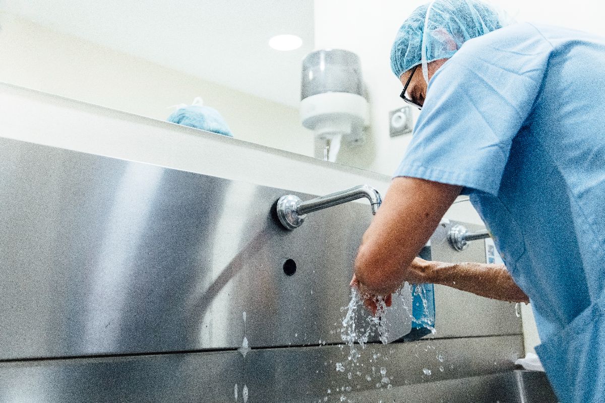 Healthcare worker in scrubs washing hands at a stainless steel hospital sink