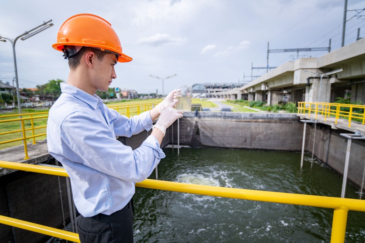 Worker in an orange hard hat testing a water sample at an industrial water treatment basin
