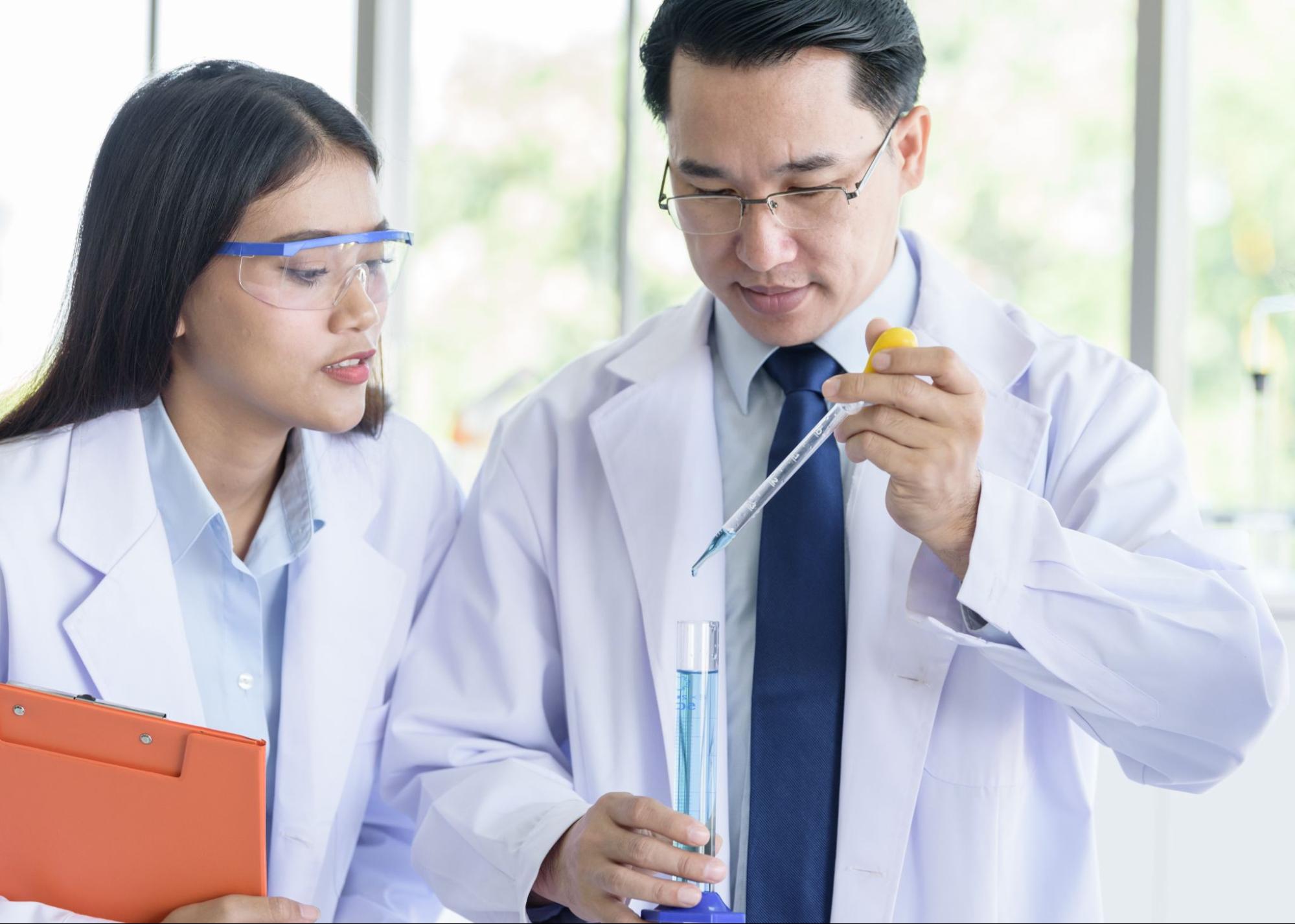 Two laboratory professionals testing a water sample with a pipette and graduated cylinder