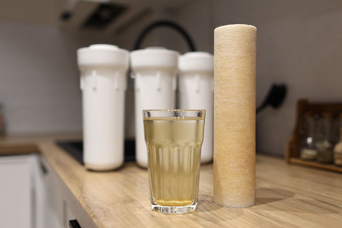 Cloudy glass of water beside a cartridge filter and countertop water filtration housings