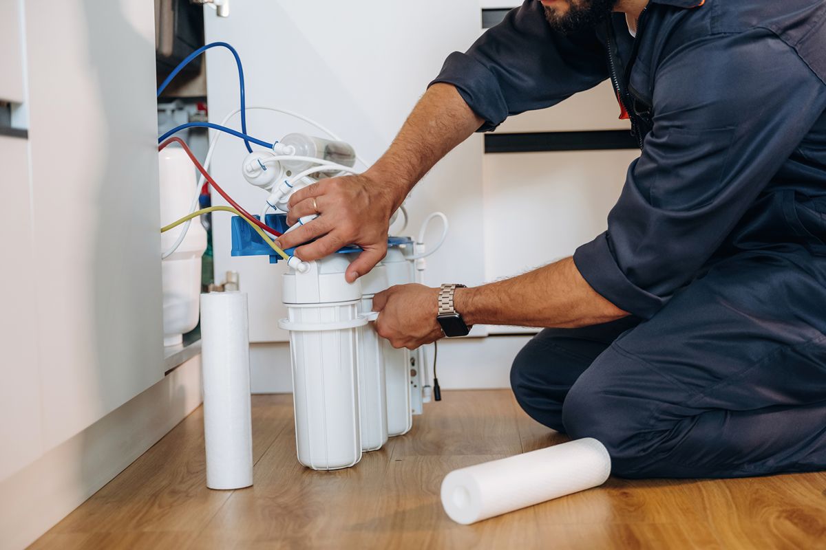 Technician servicing an under-sink reverse osmosis system with filter cartridges, tubing, and water treatment components