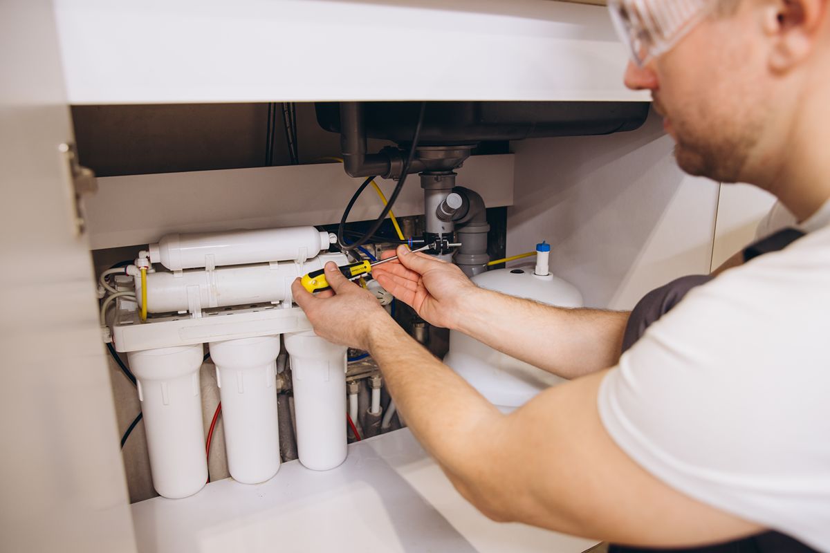 Technician checking an under-sink water filtration system for restaurant water supply maintenance