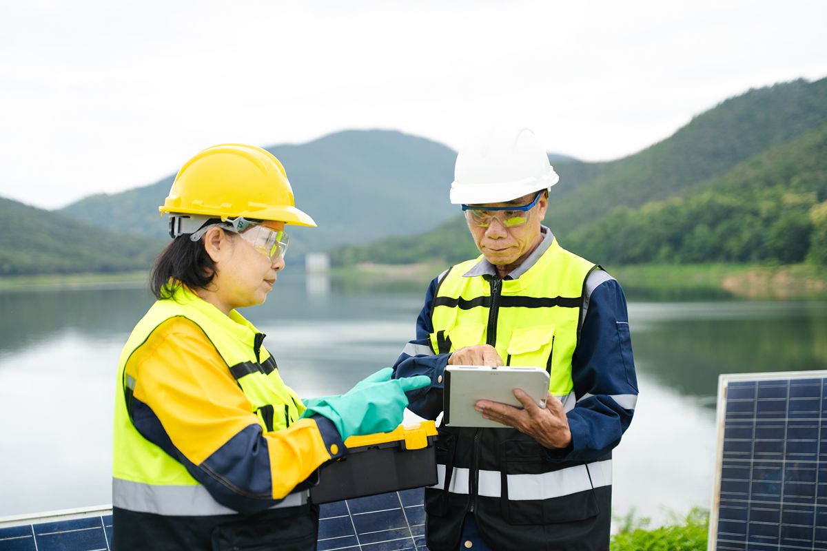 Two facility workers reviewing water treatment data near outdoor infrastructure and solar panels